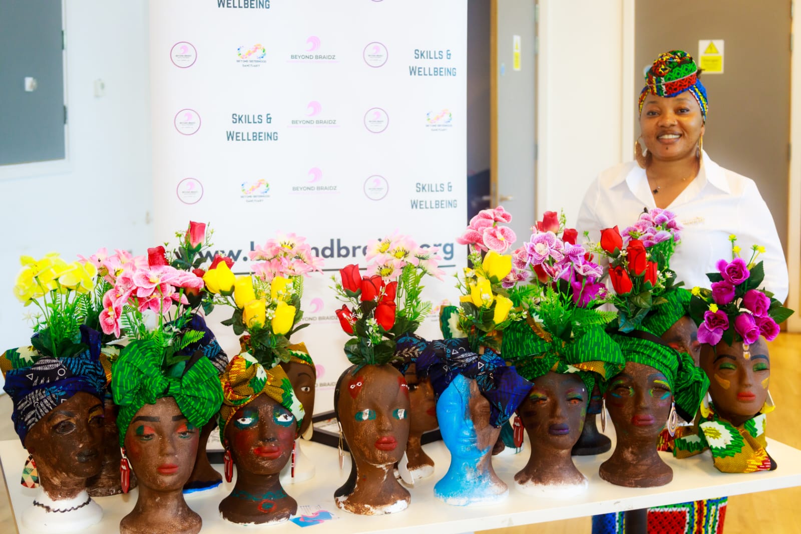 BeyondBraidz founder Bukola with a table of hand-decorated mannequin heads wearing headwraps and flowers